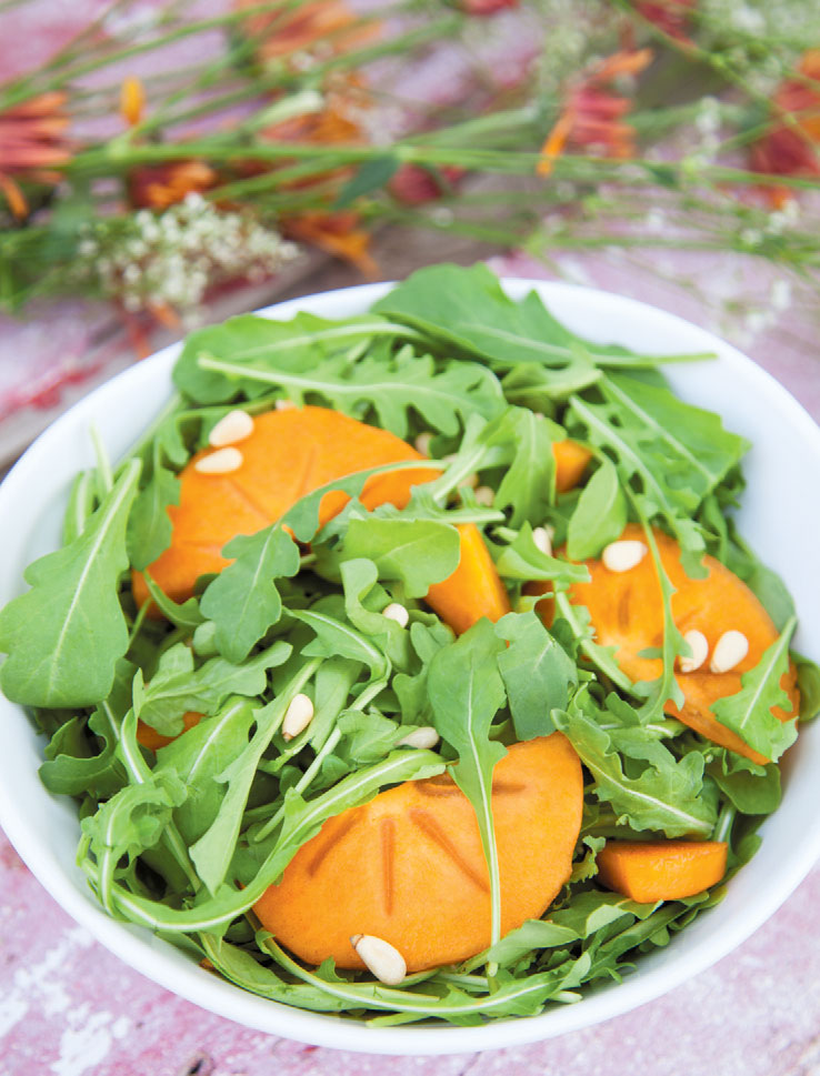 Pale pine nuts contrast with green arugula and orange fruit.